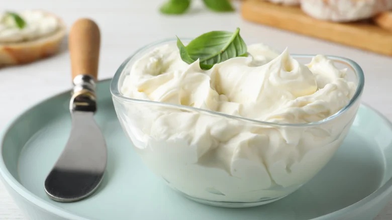 : A bowl full of cream cheese with a basil leaf on top